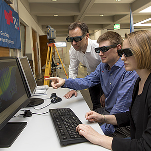 Two students and a teacher look through 3D glasses at a screen with a simulation.